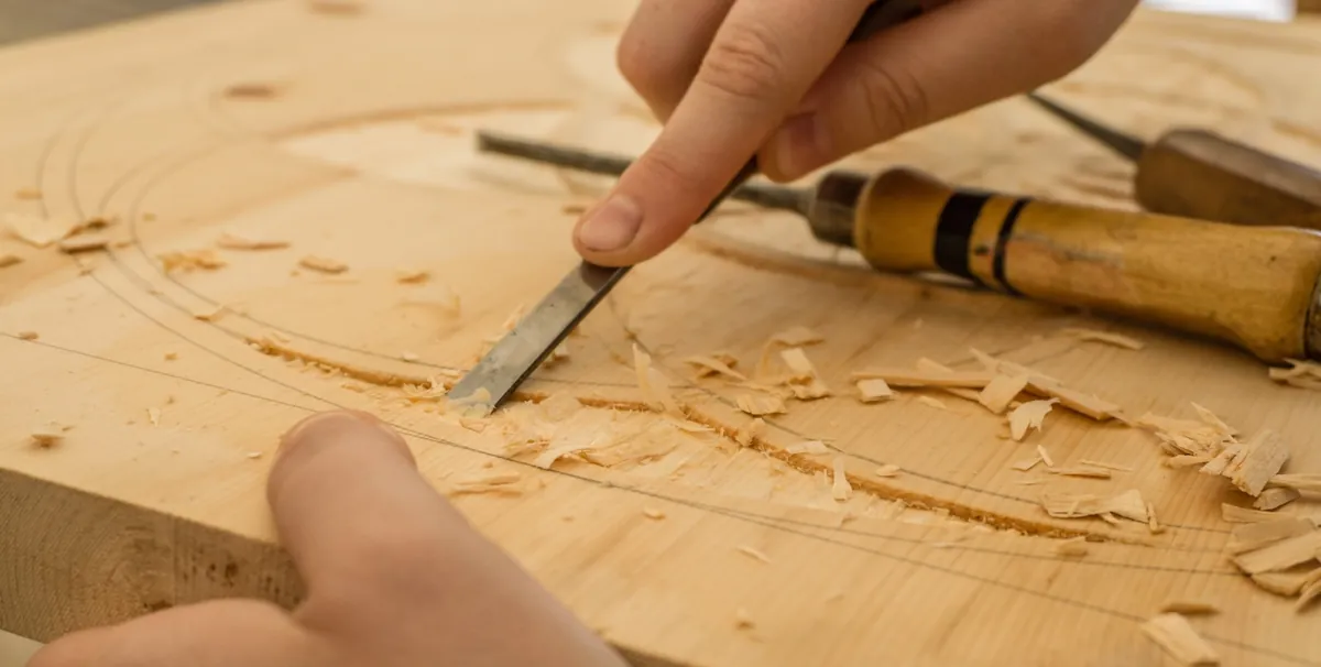 Hands guiding a chisel through fine woodwork